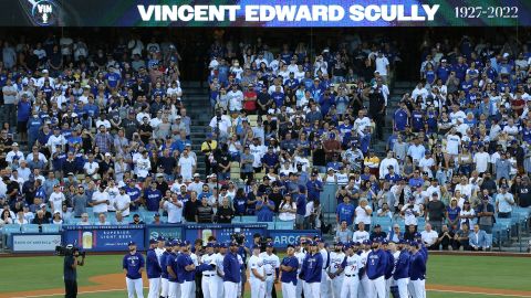 Los jugadores y entrenadores de los Dodgers de Los Ángeles se paran en el campo mientras Vin Scully es honrado durante una ceremonia previa al juego.