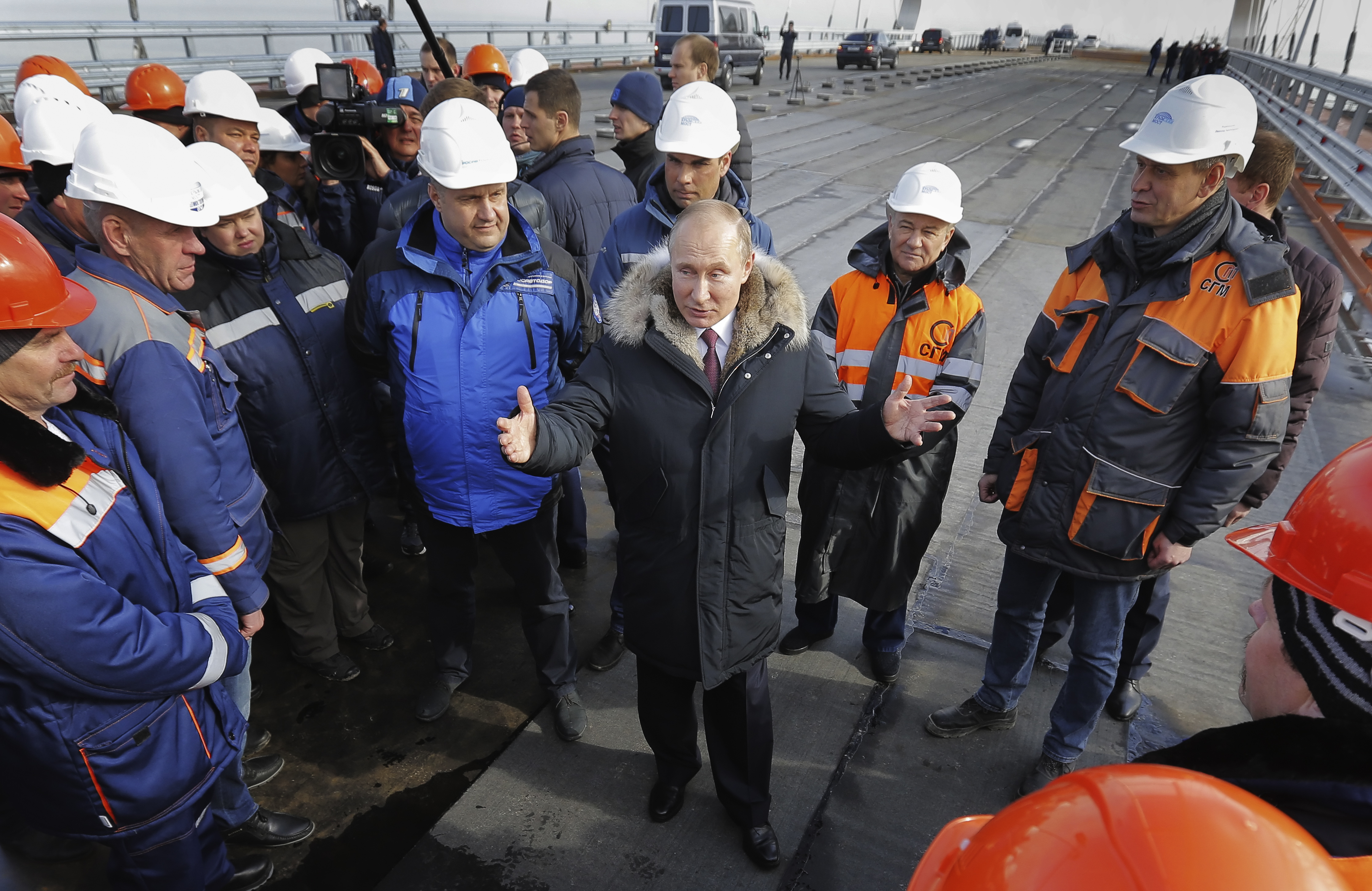 El presidente ruso, Vladimir Putin, en el centro, habla con los trabajadores que visitan la sección de carretera del puente ferroviario y de carretera que une Crimea con Rusia continental cerca de Kerch, Crimea, el 14 de marzo de 2018. Putin elogió el puente, que se completará a finales de este año. , como un gran logro de ingeniería y elogió a los involucrados en su construcción.