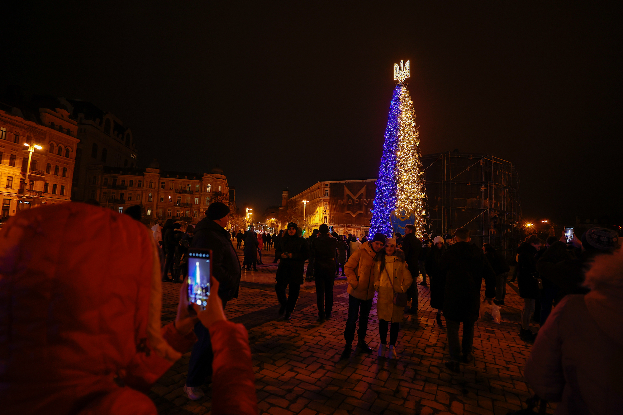 La gente toma fotos frente al árbol de Navidad recientemente iluminado en Sophia Square en Kyiv el domingo.